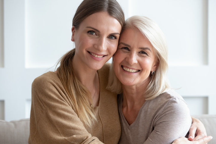 Attractive aged mother and adult daughter hugging looking at camera