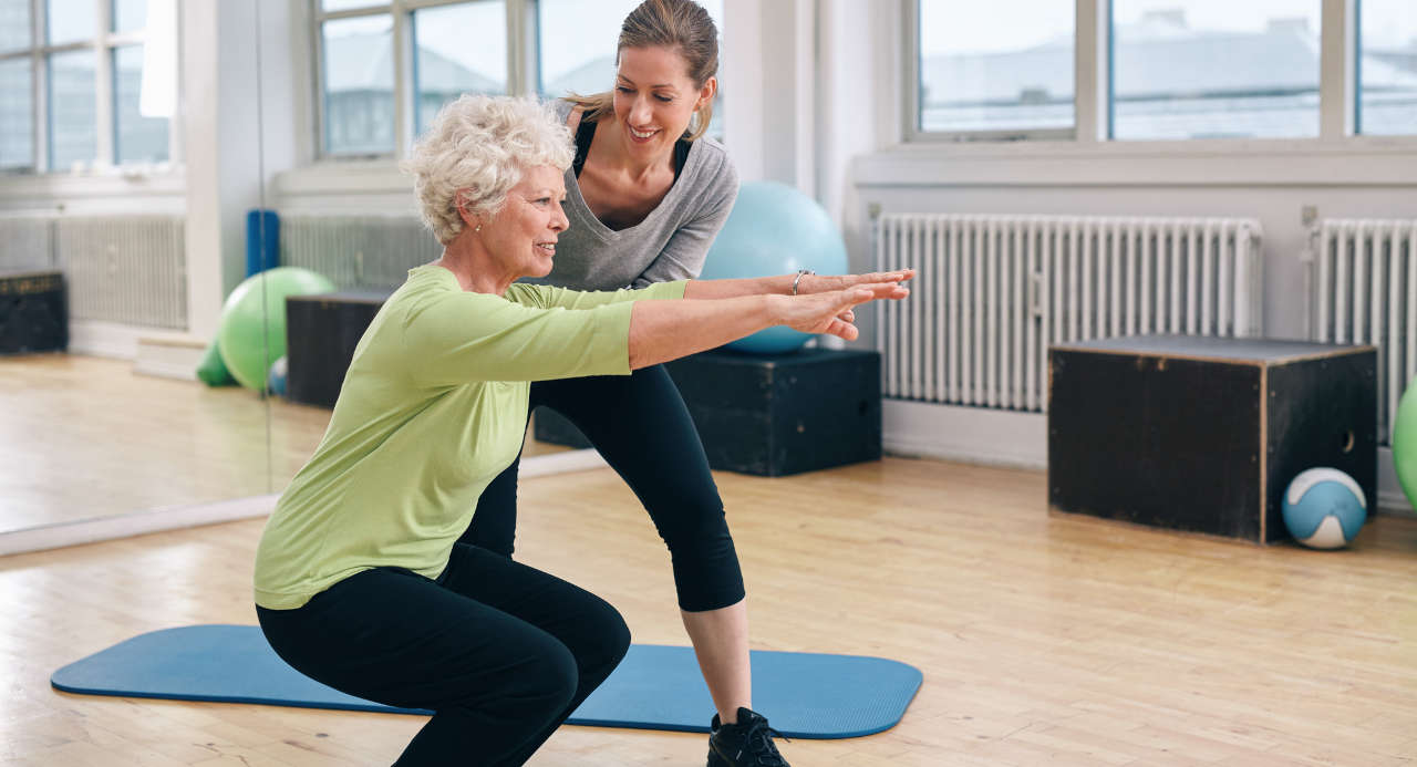 Elderly woman doing squat exercise with personal trainer to slow aging