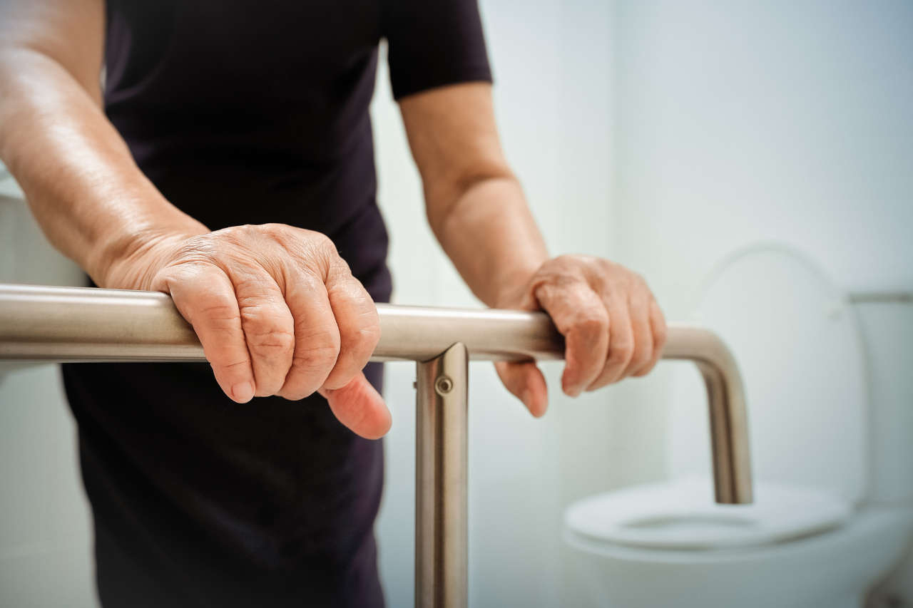 Elderly woman holding on handrail in bathroom with aging in place home modifications.