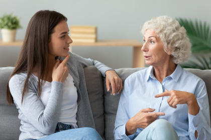 Happy grandmother chatting with granddaughter, sitting on couch together