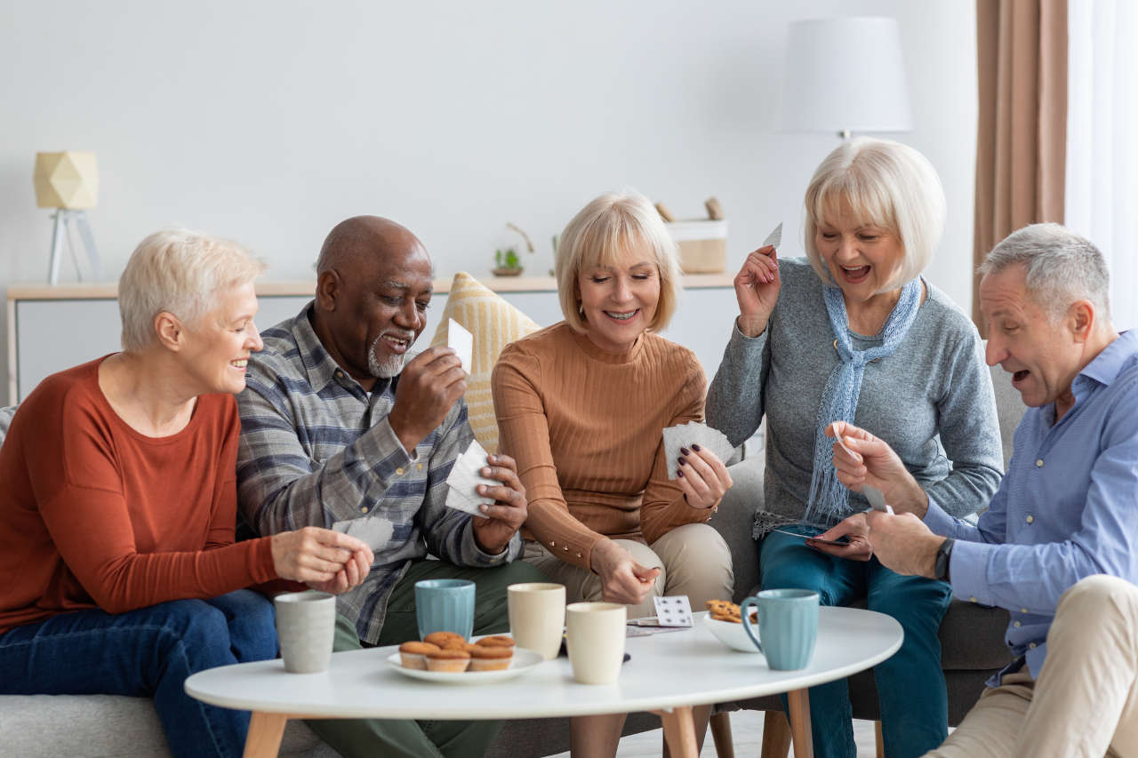 Happy senior friends playing cards at home