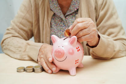 Retired elderly woman putting coins money in piggy bank and worry about monthly expenses and treatment fee payment.