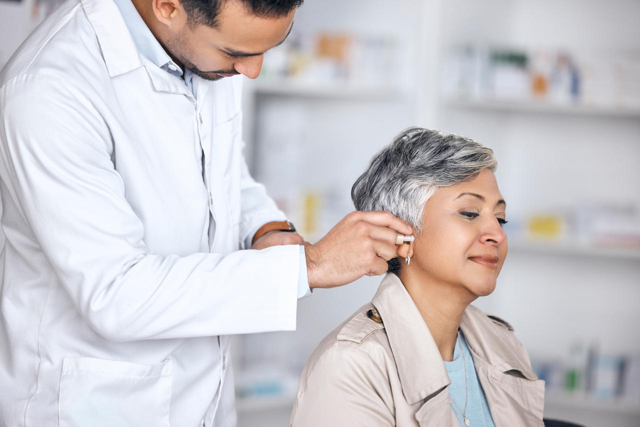 Doctor inserting hearing aid into senior’s ear